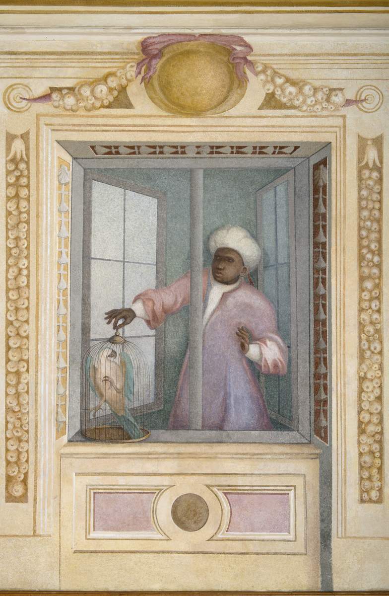 Dekoracja malarska na ścianie. Przedstawia okno dekorowane sztukateriami, a w nim czarnoskórego mężczyznę w blado-różowym ubraniu i białym turbanie na głowie, który stawia na oknie klatkę z papugą. Kolory malarstwa delikatne, pastelowe. 