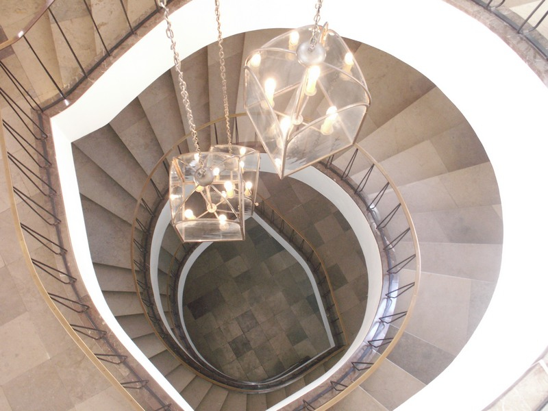 Widok od góry na klatkę schodową. Trzy przezroczyste żyrandole opadają na łańcuchach w dół. Jest to dwudziestowieczna klatka schodowa w wieży południowej.