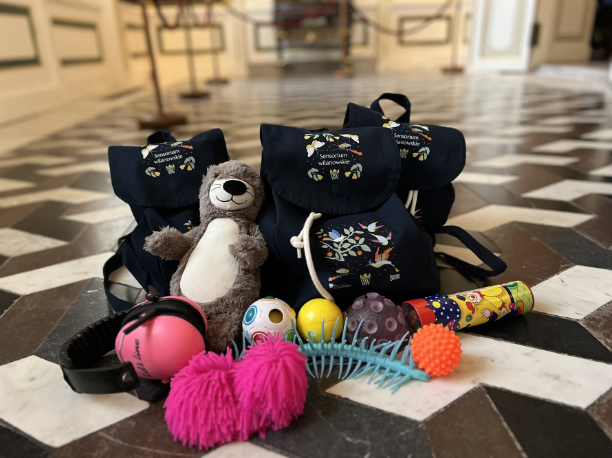 Szmaciany plecak z napisem: Sensorium Wilanowskie, wokół zabawki.
