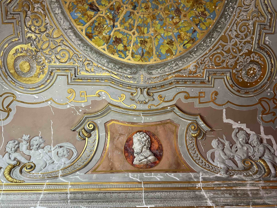 Bogato zdobiony sufit historycznego pomieszczenia. Widoczna imitacja pergoli i dekoracje rzeźbiarskie.