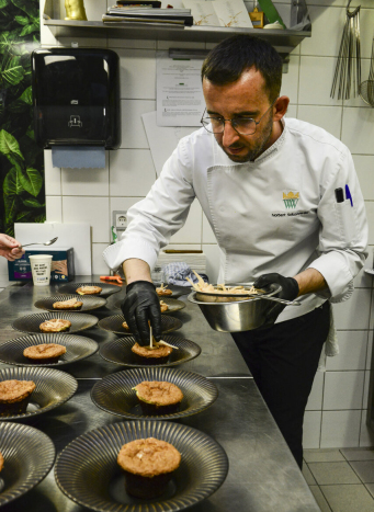 Mężczyzna w fartuchu (kucharz) w trakcie przygotowywania potraw ustawionych w takich samych talerzach.